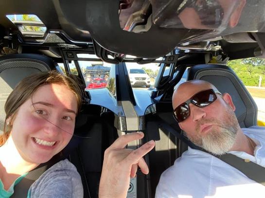 Two smiling individuals pose inside a vehicle, enjoying their time while parked in a lot.