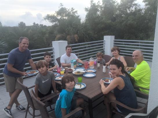 Group of family members sharing a joyful dinner on a terrace in the evening, surrounded by nature.