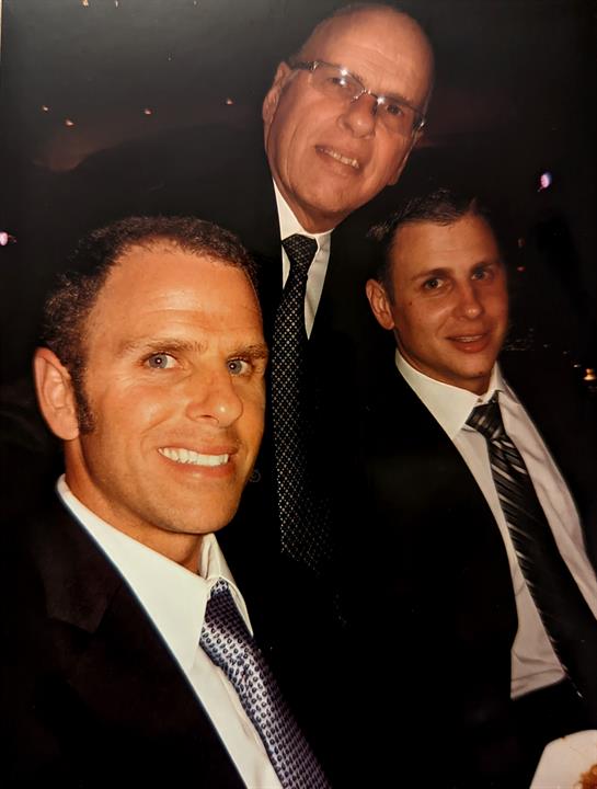 Three men are captured smiling at an elegant evening gathering, showcasing formal attire and joy.