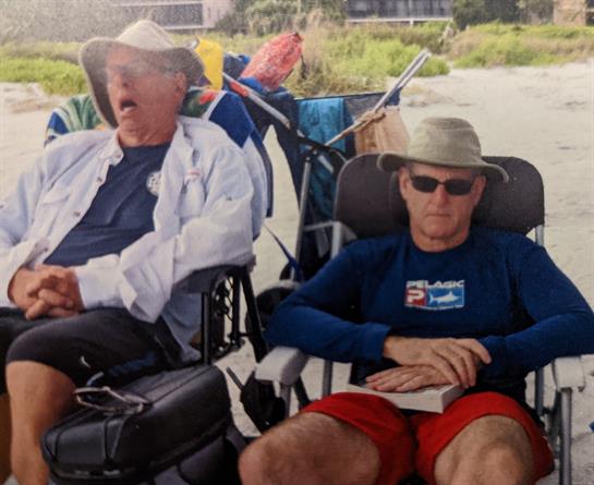 Two men are lounging comfortably in beach chairs, enjoying a sunny day by the shore.