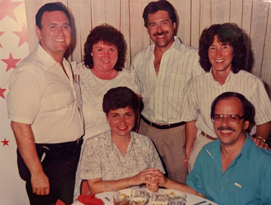 Friends gather around a table smiling and sharing stories during a casual dinner at night.