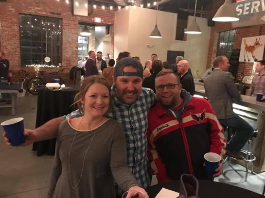 Three friends pose happily at a bustling event, celebrating and enjoying each other's company.