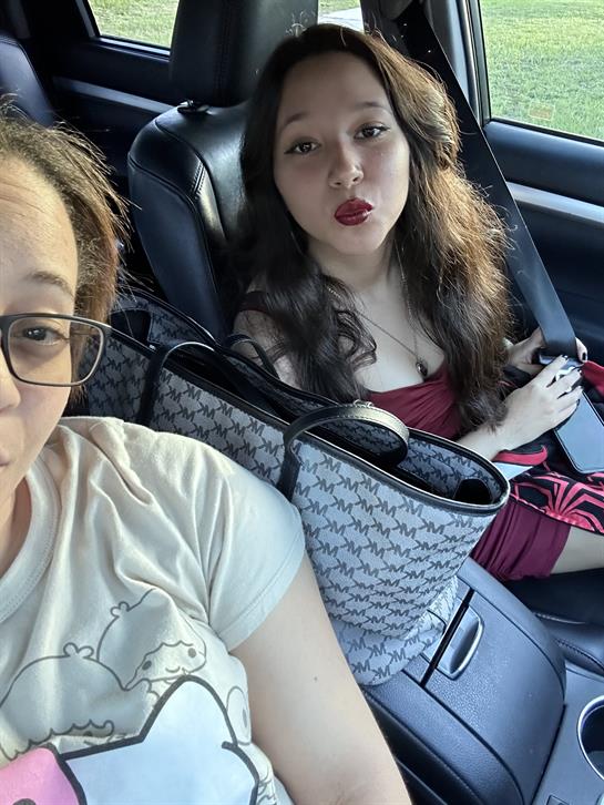 Two women are seated inside a car, smiling and posing for a selfie, enjoying their time.