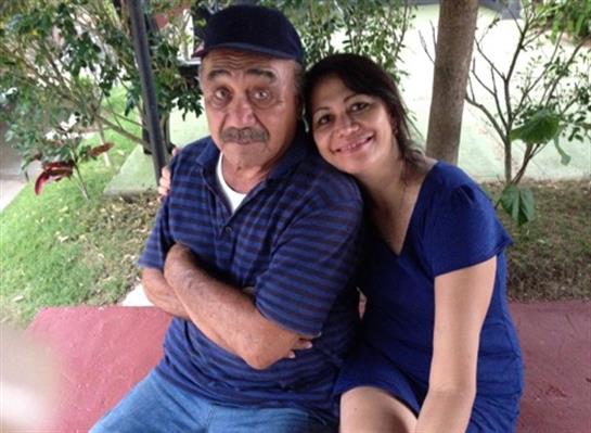 A young woman cuddles up to her grandfather, both enjoying a sunny day in a garden setting.