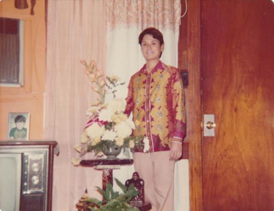 A man stands near a table adorned with fresh flowers, dressed in a vibrant traditional costume.