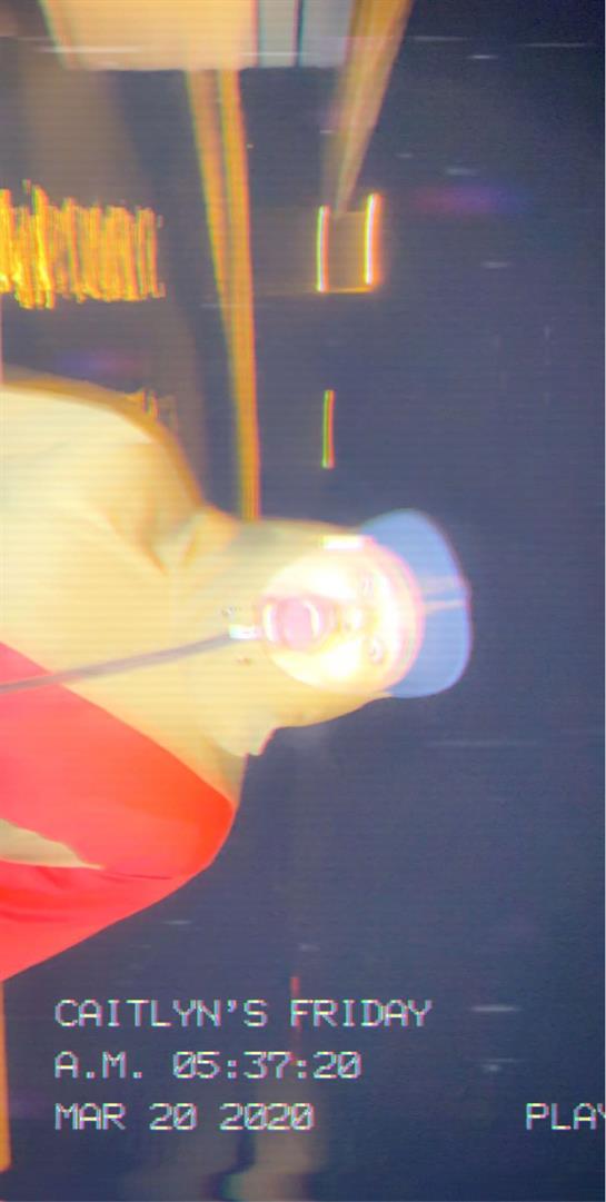 A figure in a hooded garment stands in a dark area, illuminated by a bright light source above.