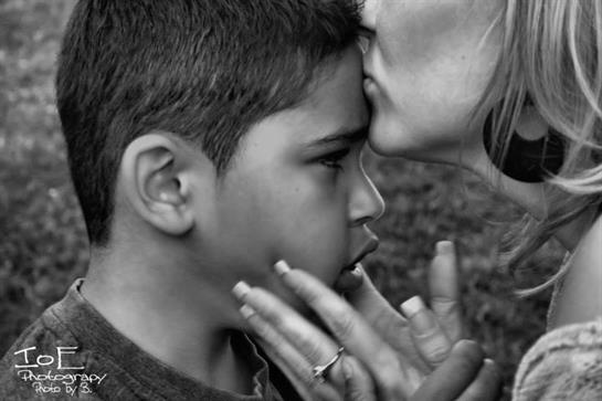 A mother affectionately kisses her son's forehead, showcasing love and connection at dusk.