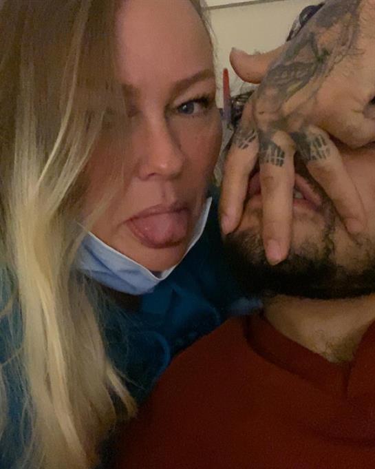 Two individuals share a playful moment, showcasing tattoo artistry and expressions of fun.