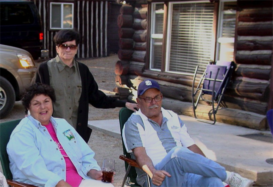 Friends relax outside a cozy cabin, sharing stories and drinks while enjoying the warm afternoon.