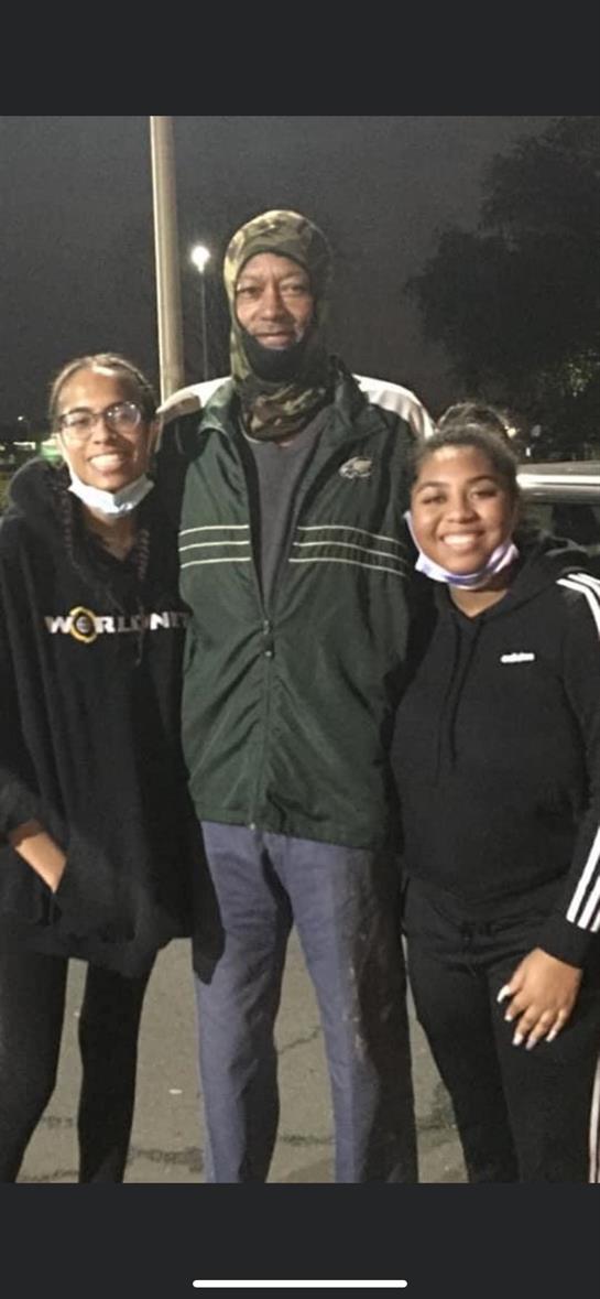 Three friends share a joyful moment while wearing masks during a night event outside.