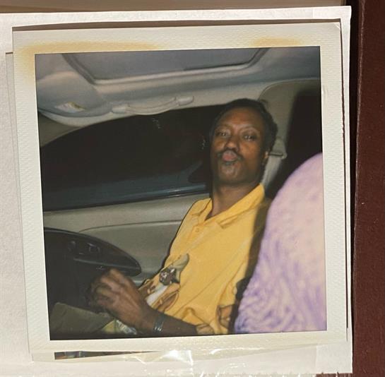 A man is seated in a car, sharing a light moment with a passenger at night.