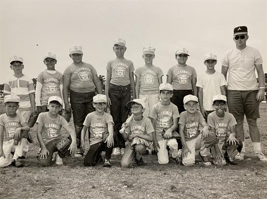 Group of young baseball players gather outdoors, showing team spirit with matching shirts and caps.