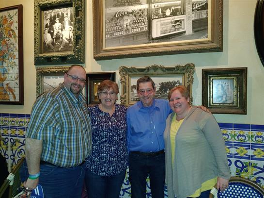 Four friends stand together in a warmly decorated room filled with framed artwork and memories.