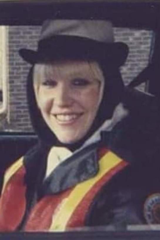 A woman wearing safety gear smiles while seated inside a vehicle, ready for work.