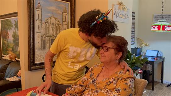 A young man leans in to kiss an older woman on the forehead while both smile happily.