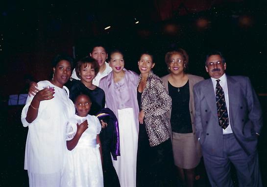 A joyful family gathering showcases eight individuals in elegant clothing, celebrating together.