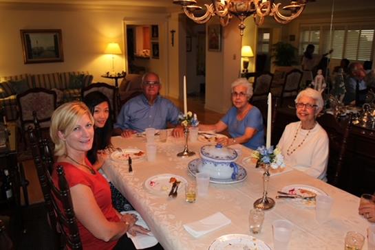 A group of five people enjoying a meal together in a cozy dining room. Candles illuminate the table.