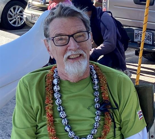 A cheerful elderly man wearing a green shirt and leis participates in a festive outdoor gathering.