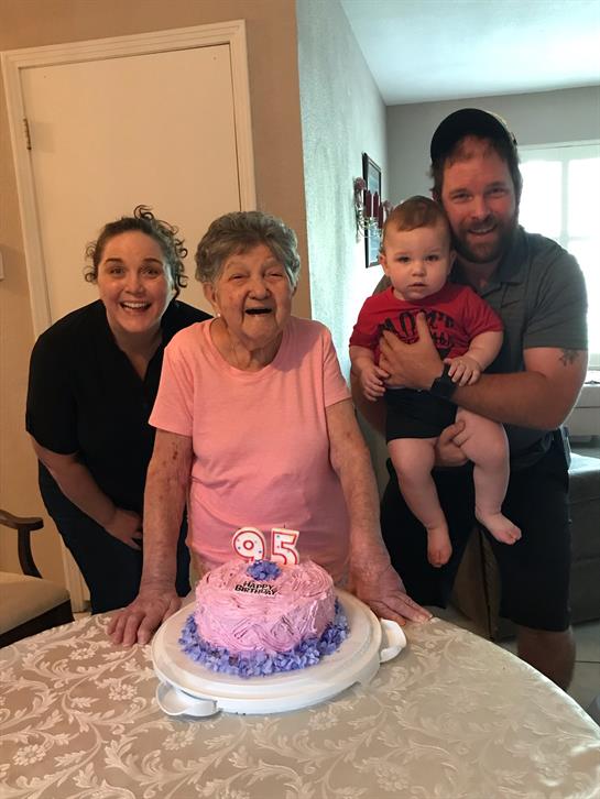 Family gathers around to celebrate a 95th birthday with cake and smiles in a warm home environment.