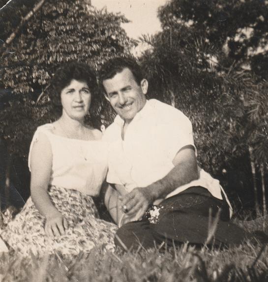 Couple sits closely in a serene outdoor environment, smiling happily amid the greenery.