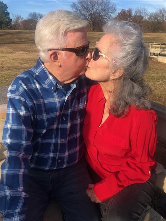Couple enjoys a romantic moment in a park, exchanging a heartfelt kiss while basking in sunlight.