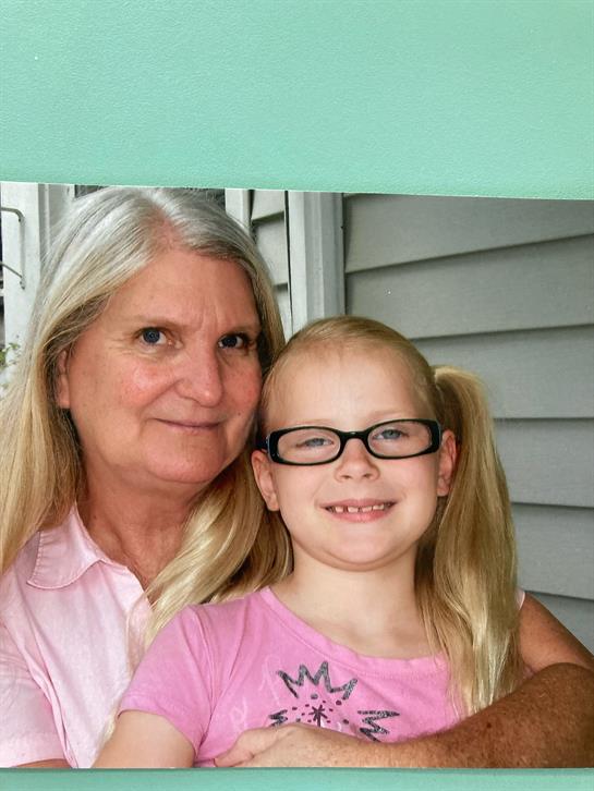A grandmother hugs her granddaughter, both smiling happily while enjoying a warm day outdoors.