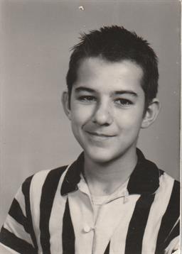 Boy smiles in a striped shirt, exuding cheer, likely in a school setting.