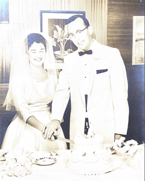 Wedding couple cuts a beautiful cake while guests gather around in a decorated hall.