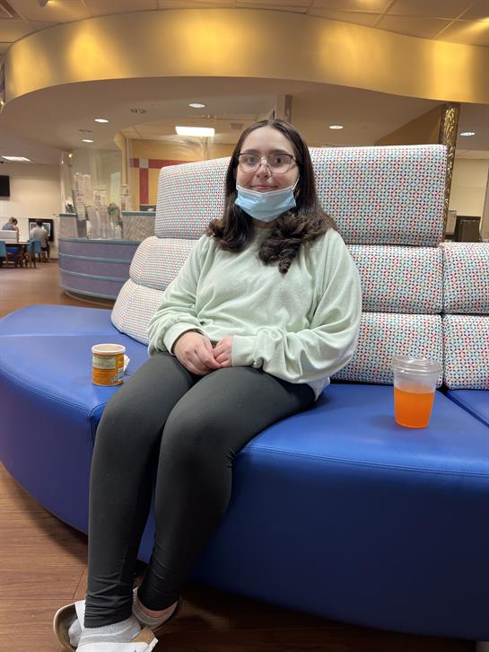 A young individual sits comfortably on a colorful couch with drinks nearby, enjoying the atmosphere.