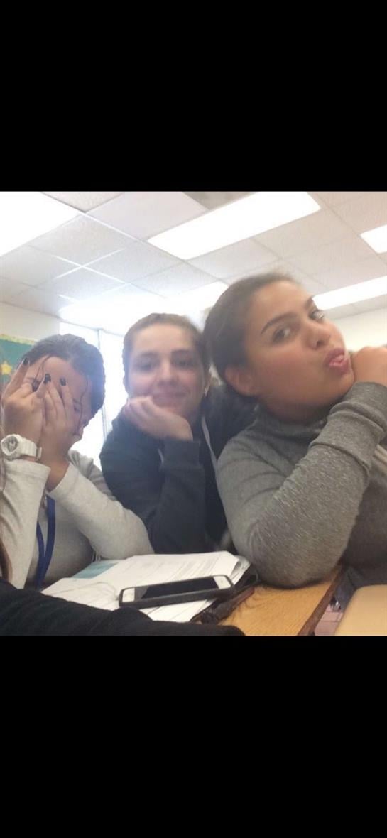 Four students are sharing a fun moment at their desks while engaging in light conversation.