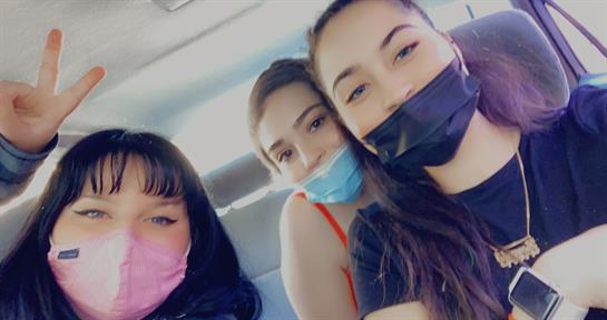 Three friends smile at the camera, wearing various face masks inside a vehicle, enjoying their time.