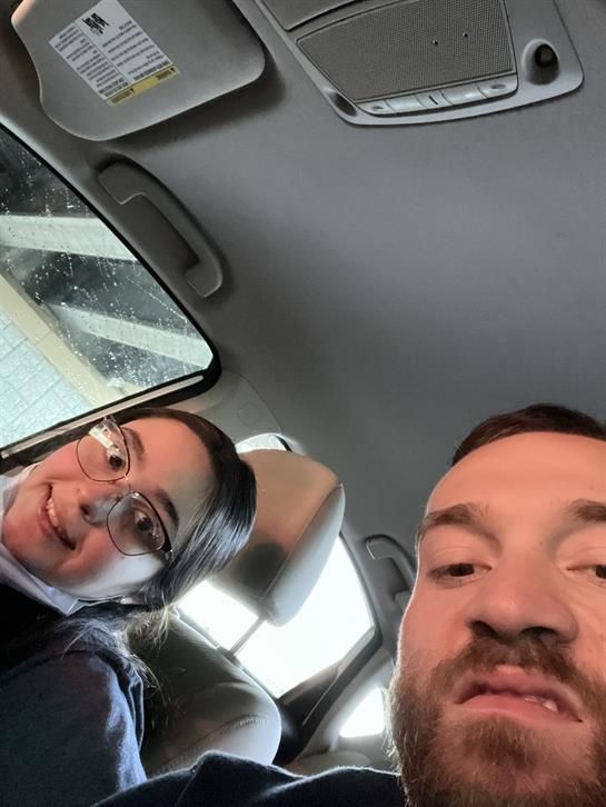 A couple smiles while sitting in a car, engaged in a cheerful moment together, rain outside.
