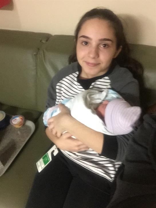 A girl smiles as she cradles a newborn baby in a cozy living room setting.