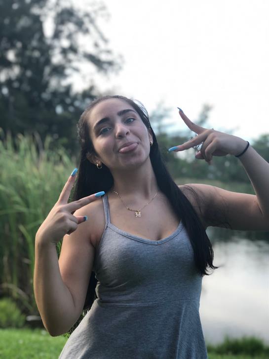 A young woman joyfully poses by a serene water feature amidst lush greenery.