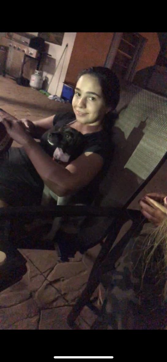 A child holds a small dog close while engaging with family in a relaxed indoor atmosphere.