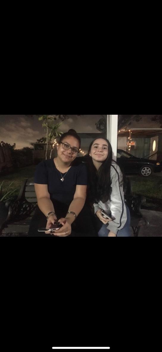 Two friends relax on a bench in a backyard, sharing laughter and using their smartphones.