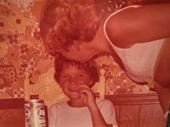 A joyful child receives affection from a mother in a colorful kitchen filled with warmth.