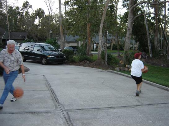 Two children run joyfully while playing tag in a driveway filled with trees.