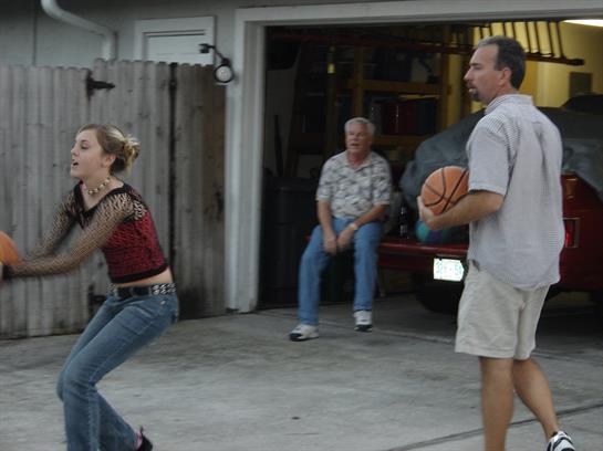 A woman prepares to shoot a basketball while a man waits to receive the ball; a spectator observes.