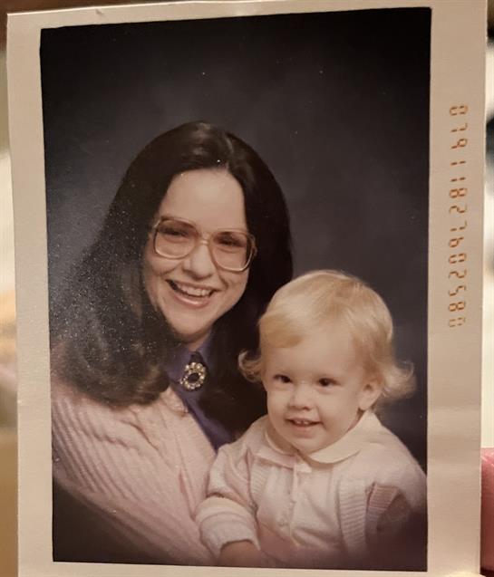 A woman with glasses smiles joyfully while holding a young child in a cozy studio.