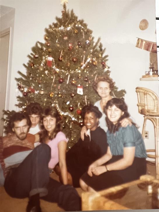 Six friends gather around a beautifully decorated Christmas tree, enjoying the festive spirit.