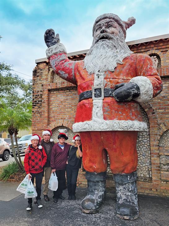 Group of friends poses with giant Santa statue, celebrating the holiday spirit in a charming town.