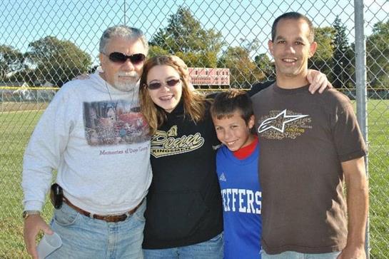 Group of four people stands together at a soccer field, smiling and enjoying the day outside.