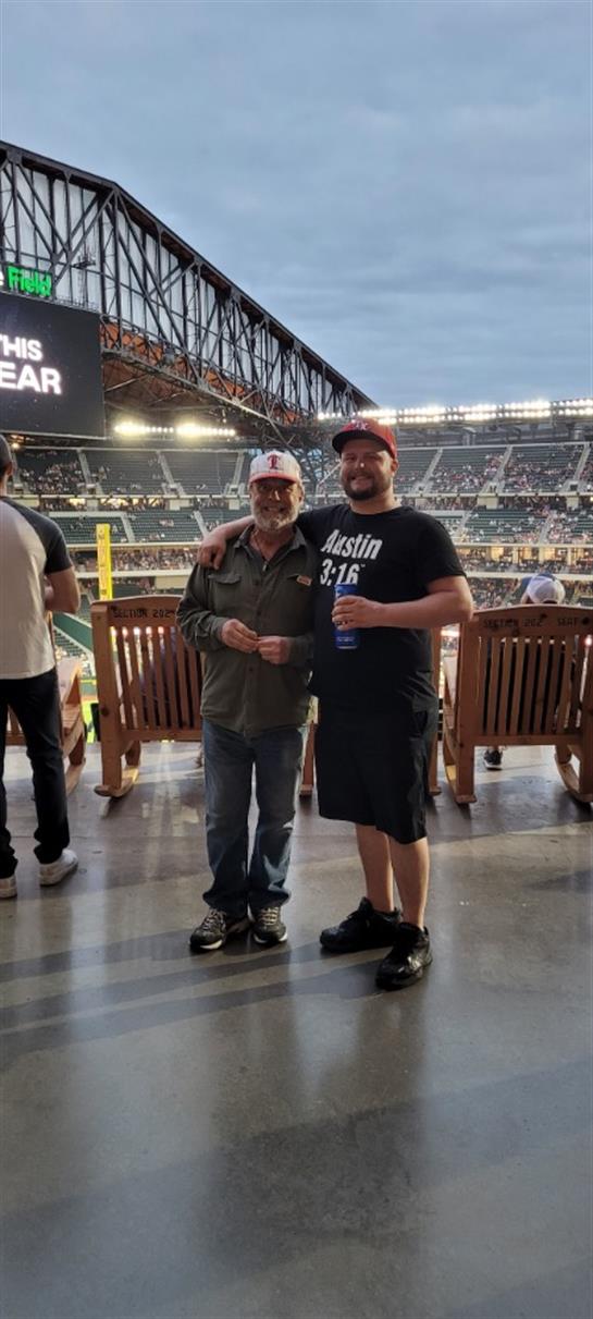 Two friends smile and hold drinks at a lively stadium, enjoying the atmosphere.