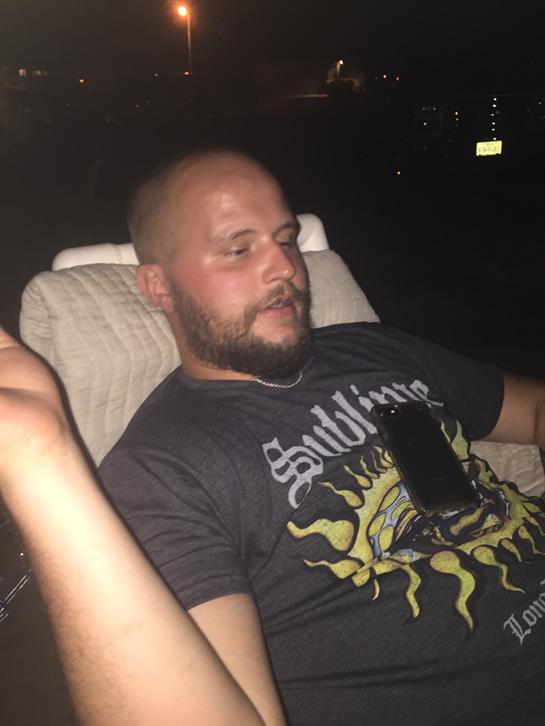 Friends gather by the water at night, engaging in relaxed conversation while enjoying music.