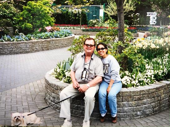 A couple relaxes on a stone bench surrounded by lush flowers and plants, enjoying the day.