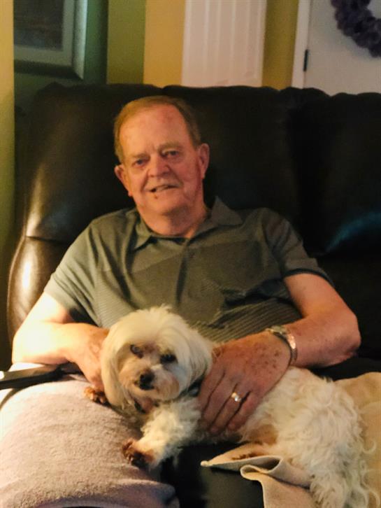 An elderly man enjoys a peaceful moment on his couch with a small dog resting on his lap.