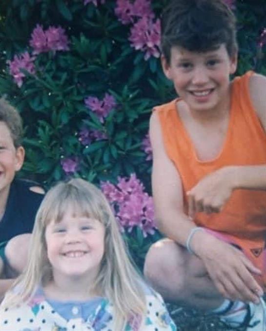 Three children enjoy playful moments together in a colorful garden filled with flowers.