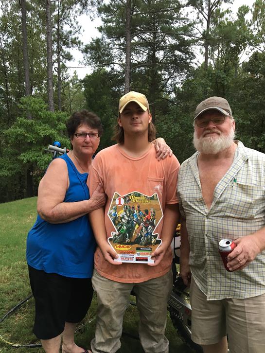 Family poses together to commemorate a notable achievement outdoors on a sunny day.