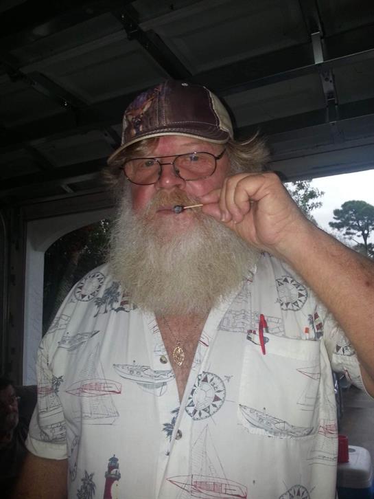 Bearded man smiles while holding a toothpick at home in a relaxed atmosphere during the evening.